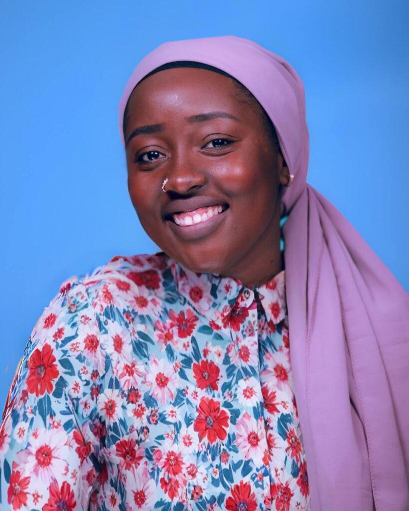 Smiling Black woman wearing a floral shirt and lavender headscarf, posing in front of a blue background — founder of Free AI Prompts, a blog sharing expert AI prompt engineering tips and tools.